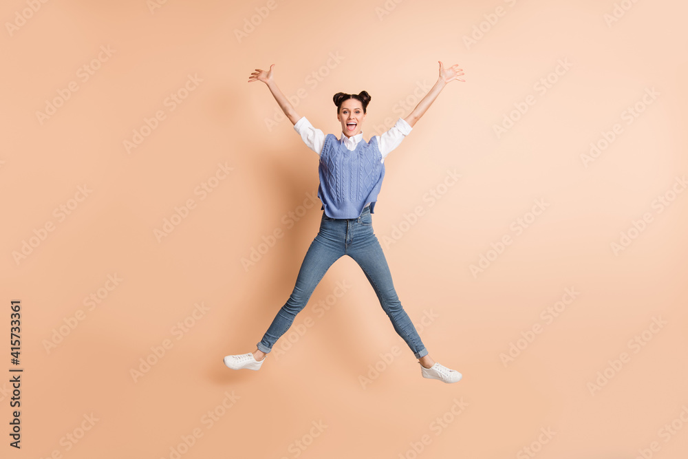 Full size photo of brunette optimistic lady jump wear white shirt blue vest jeans sneakers isolated on beige color background