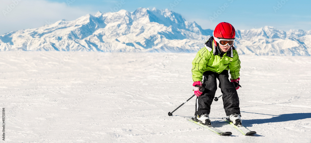 Happy child with helmet and goggles on the ski slopes at high altitude..In the background the Alps