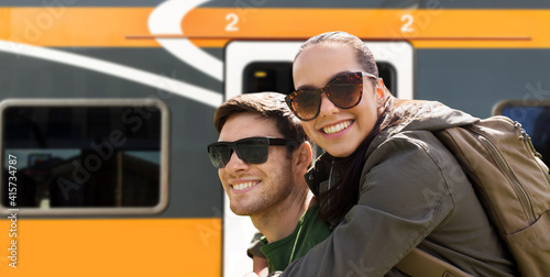 travel, tourism and people concept - happy young couple with backpacks traveling over train on railway station on background