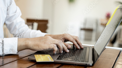 A man holds a credit card and uses a laptop. He is filling out credit card information for online shopping  credit cards can be used to pay for goods and services through physical stores and online.
