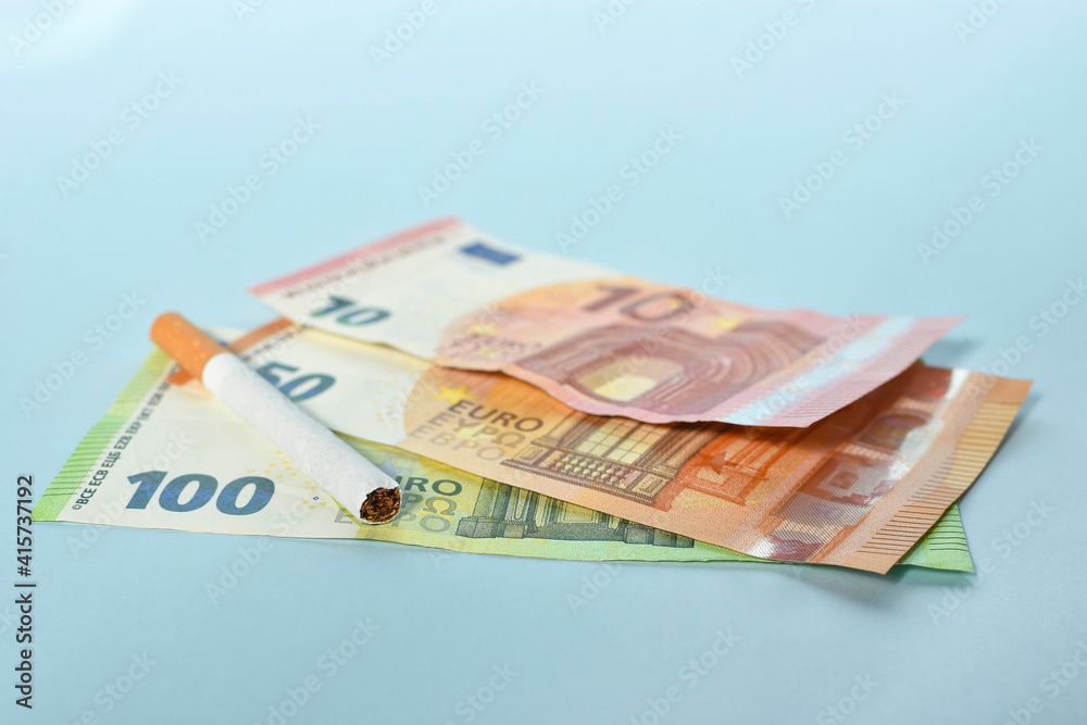 Cigarettes and money on blue background. Euro banknotes and coins, cost of smoking, cigarette price concept. Selective focus Cigarettes and money on blue background. Euro banknotes and coins, cost of smoking, cigarette price concept. Selective focus