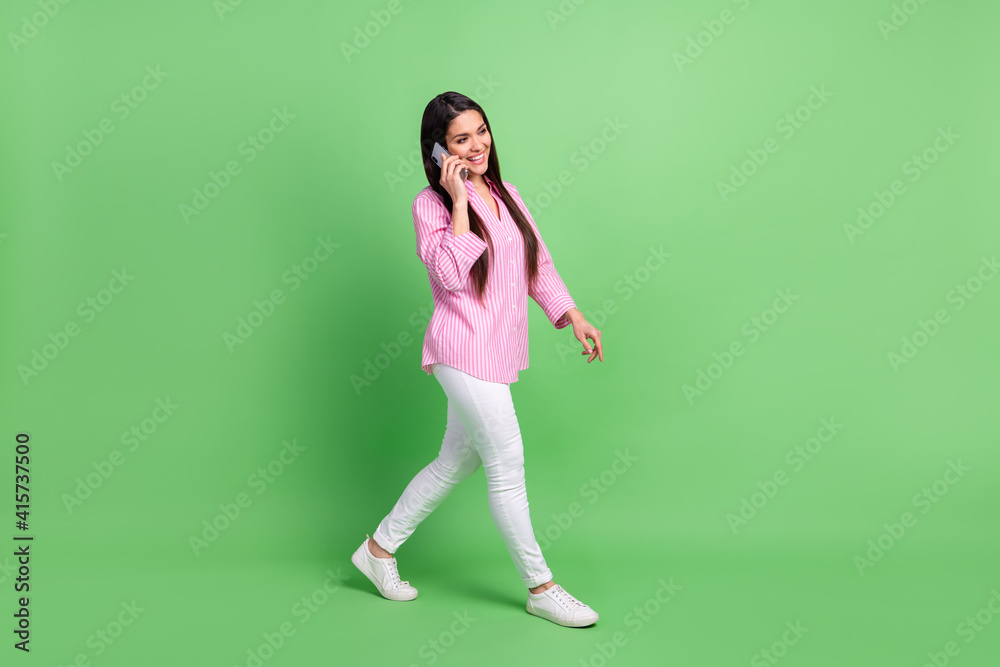 Full length body size view of attractive cheerful girl going talking on phone operator roaming isolated over green pastel color background Full length body size view of attractive cheerful girl going talking on phone operator roaming isolated over green pastel color background
