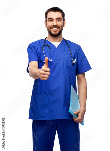healthcare, profession and medicine concept - happy smiling doctor or male nurse in blue uniform with folder showing thumbs up over white background
