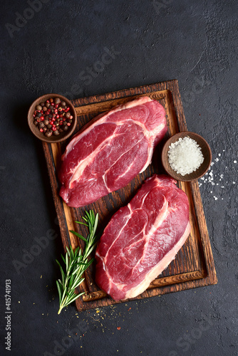 Raw organic marbled beef steaks with spices  on a wooden cutting board . Top view with copy space.