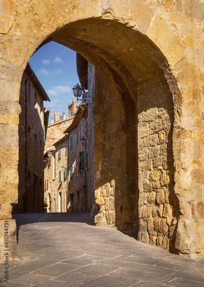 View of a medieval alley through wall gate, San Quirico d'Orcia, Italy