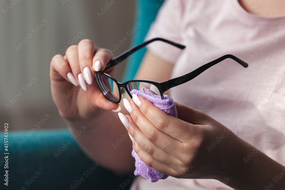 Young woman cleaning eyeglasses with a napkin while sitting in a chair Young woman cleaning eyeglasses with a napkin while sitting in a chair
