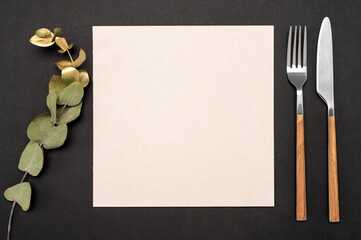 Mockup Blank card and cutlery. Knife and fork with white paper for menu or recipe text and gold eucalyptus branch. Flat lay with mockup food menu on black table