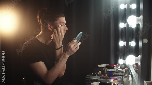 Drag artist - young man puts makeup behind the scenes in front of a mirror