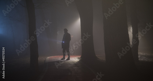 detective with a flashlight in the forest at night in the fog