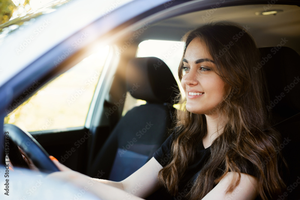 Beautiful young modern girl driving a car on sunny summer day. Female driver alone in the car, close-up, sun on the background. Beautiful young modern girl driving a car on sunny summer day. Female driver alone in the car, close-up, sun on the background.