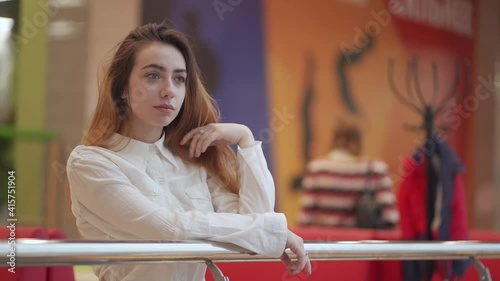 A lovely young woman in a white shirt stands outside a cafe in a shopping center.