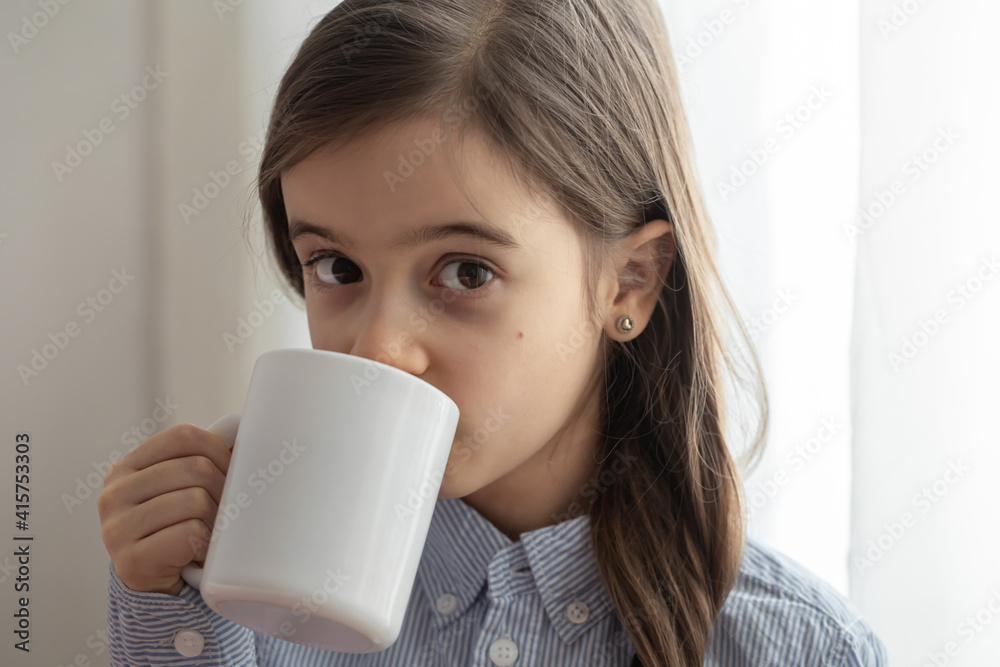 Little girl drinking from a white cup and looking at the camera close up. Little girl drinking from a white cup and looking at the camera close up.