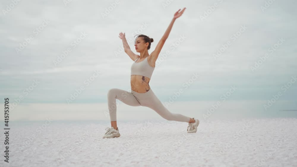 Young woman training in nature on the beach in front of dry lake and cloudy sky. Morning gymnastic exercises. Healthy active lifestyle concept. High quality 4k footage Young woman training in nature on the beach in front of dry lake and cloudy sky. Morning gymnastic exercises. Healthy active lifestyle concept. High quality 4k footage