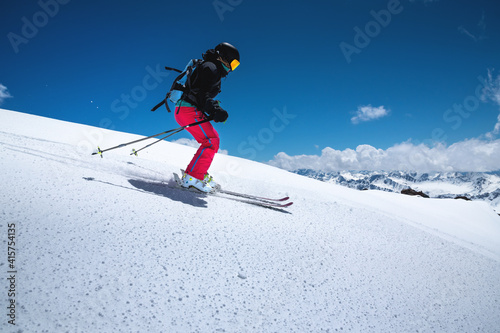 A freerider skier in red pants with a rockzack rides down a snowy slope in cloudy weather. Womens freeride sports background