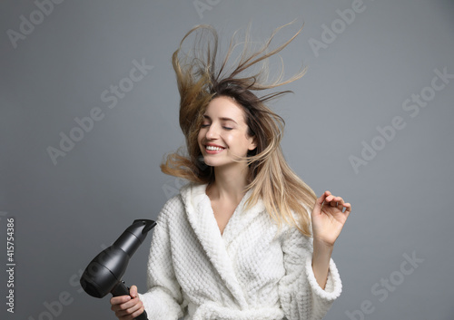 Beautiful young woman using hair dryer on grey background