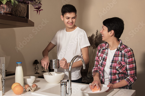 Obraz na płótnie Happy smiling mother and son on kitchen. Teenage boy helping to cook food, mom washing the dishes. Concept of friendly relationship between parents and children teenagers. w salonie