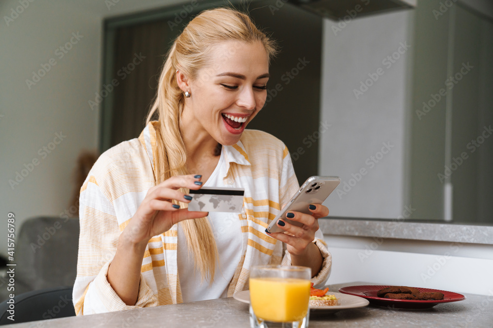 Excited woman using cellphone and credit card while having breakfast Excited woman using cellphone and credit card while having breakfast