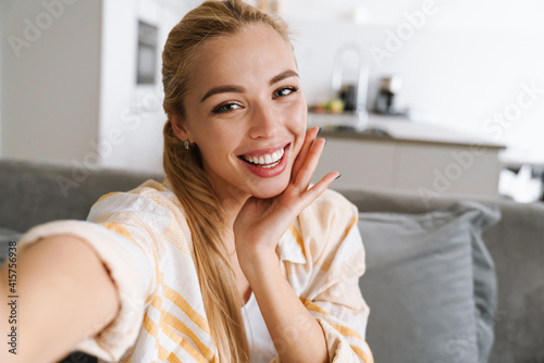 Happy blonde woman smiling while taking selfie photo at home