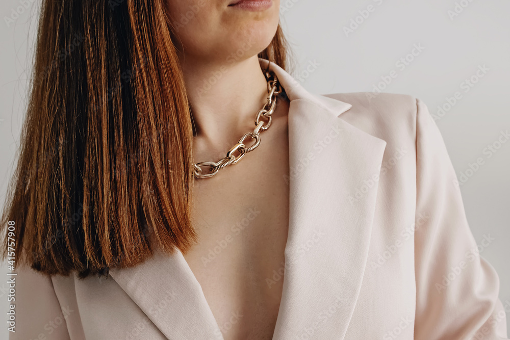 Woman in light beige jacket wearing golden chain necklace.