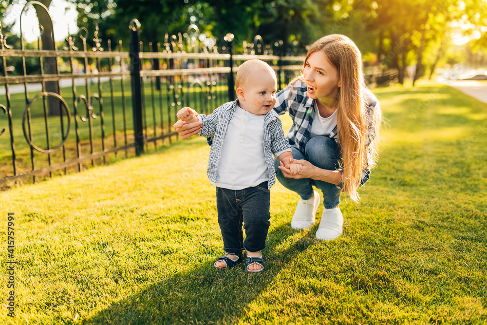 Fototapeta premium Mother helps her child learn the first step on the lawn
