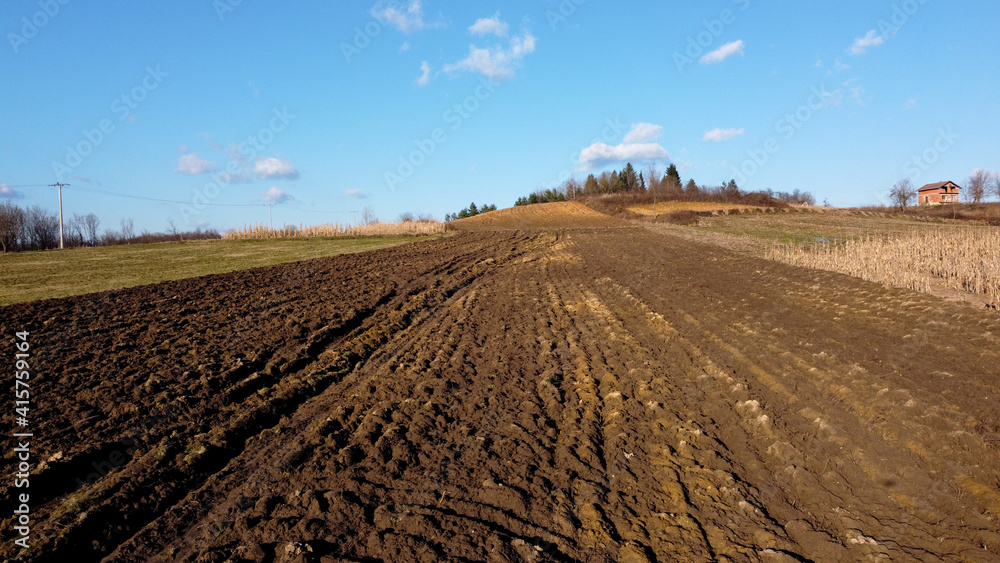 Arial drone view of freshly plowed field ready for seeding and planting in spring. Farmland. Empty plowed farm land prepared for the new crop. Agriculture. Brown soil near village. Arial drone view of freshly plowed field ready for seeding and planting in spring. Farmland. Empty plowed farm land prepared for the new crop. Agriculture. Brown soil near village.