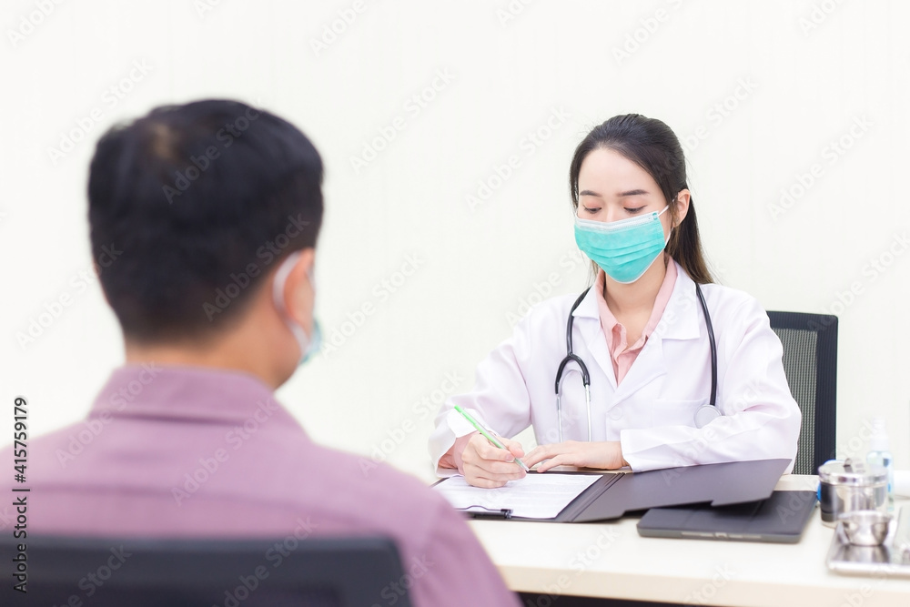 An Asian female doctor is inquiring about a male patient's illness. In the hospital examination room, she wears medical face mask to prevent Coronavirus disease in hospital. Health care concept. An Asian female doctor is inquiring about a male patient's illness. In the hospital examination room, she wears medical face mask to prevent Coronavirus disease in hospital. Health care concept.