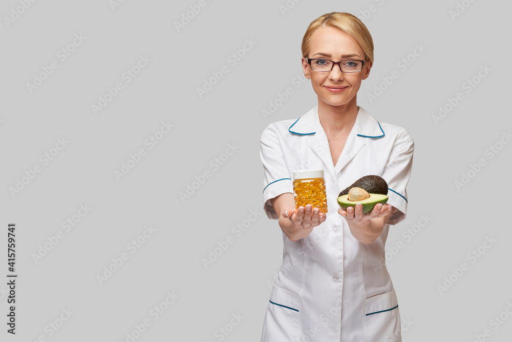 Health care and diet concept - doctor nutritionist or cardiologist holding fish oil in capsules for vitamin D and omega-3 fatty acids and avocado Health care and diet concept - doctor nutritionist or cardiologist holding fish oil in capsules for vitamin D and omega-3 fatty acids and avocado