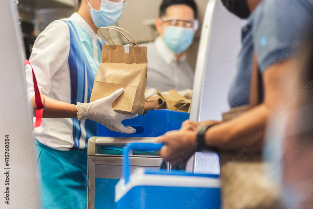 Flight attendant in face mask with gloves giving meals to the passenger travel bubble.