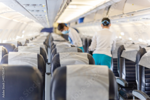 Blurred conceptual flight attendant in face mask checking the passenger seat. © bignai