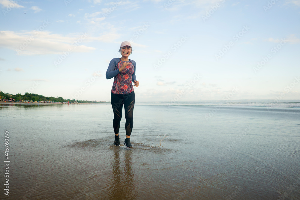 fit and attractive mature woman with grey hair doing beach workout on her 50s running on the beach happy and free in senior fitness selfcare and wellness concept