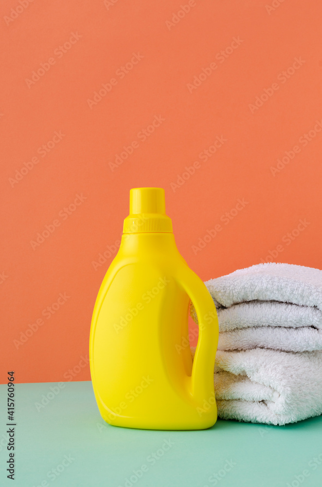 Vertical image.Yellow container of kid`s laundry detergent and white stack of towels on the blue surface against orange background Vertical image.Yellow container of kid`s laundry detergent and white stack of towels on the blue surface against orange background