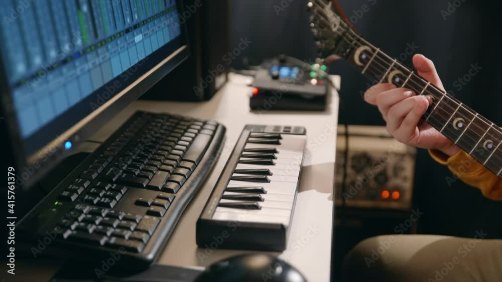 Close up male hands of musician recording song in record studio. Man playing guitar and synthesizer creating music using equalizer program.