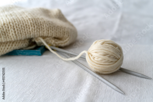 Grey knitting needles with knitting made thick wool yarn on white background with soft focus. Female hobby and leisure knitting concept.