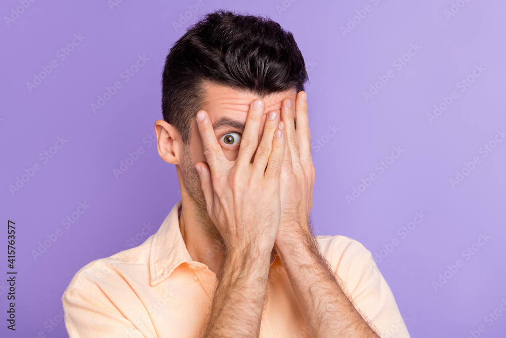 Photo of shy scared anxious young man palm cover face peering wear beige shirt isolated purple color background Photo of shy scared anxious young man palm cover face peering wear beige shirt isolated purple color background
