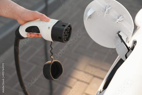 Schilderij op canvas Woman inserting plug into electric car socket at charging station, closeup