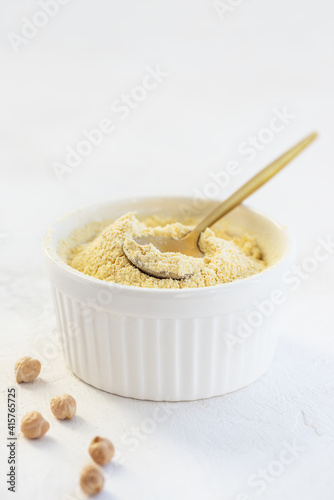 Chickpea flour with a spoon in a white bowl on a light background.
