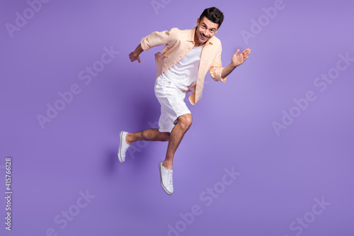 Full size profile photo of optimistic brunet guy jump run wear peach shirt shorts footwear isolated on lilac background