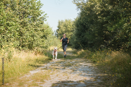  woman running with a dog. Canicross exercises. Healthy lifestyle concept. Woman with an American Bulldog at the lake. Friendship between humans and animals