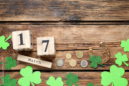 Flat lay composition with clover leaves and block calendar on wooden table, space for text. St. Patrick's Day celebration