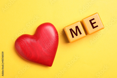 Phrase Love Me made with cubes and heart on yellow background, flat lay