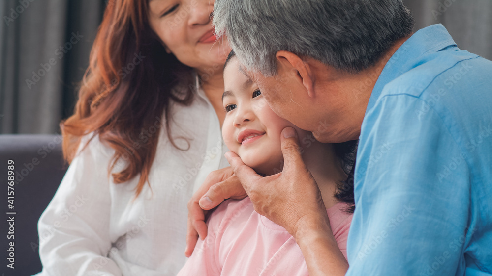 Asian grandparents kiss granddaughter cheek at home. Senior Chinese, old generation, grandfather and grandmother using family time relax with young girl kid lying on sofa in living room concept. Asian grandparents kiss granddaughter cheek at home. Senior Chinese, old generation, grandfather and grandmother using family time relax with young girl kid lying on sofa in living room concept.