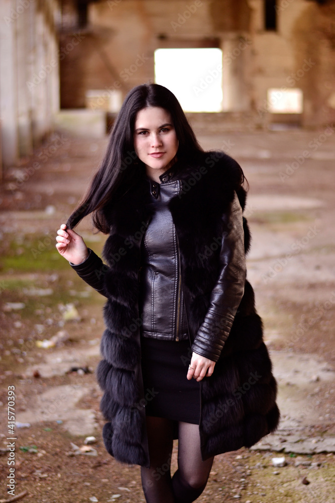Young, beautiful brunette with long hair in a fur coat in an abandoned building