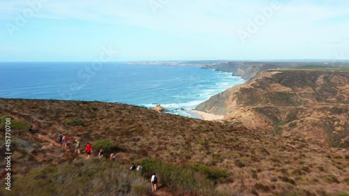 Aerial flyover mountain with hiker group and beautiful atlantic ocean landscape with sandy beach in background. Algarve Coastline in Portugal.