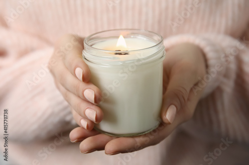 Fototapeta Woman holding burning candle with wooden wick, closeup