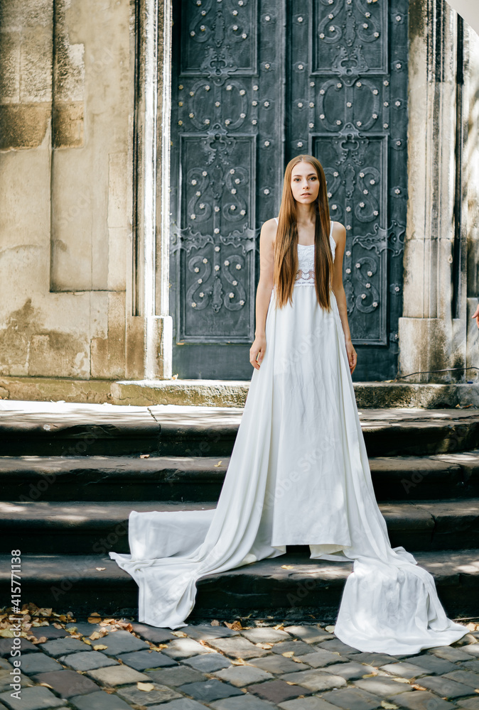 Young romantic elegant girl in long white dress posing over ancient door