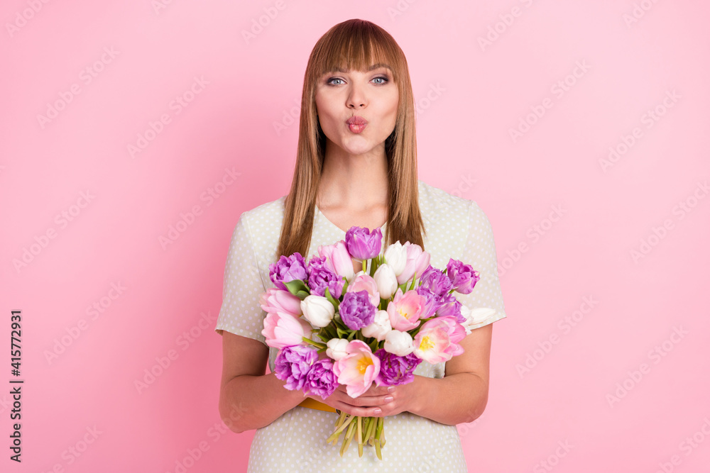Portrait of attractive girl holding in hands flowers congrats sending air kiss isolated over pink pastel color background