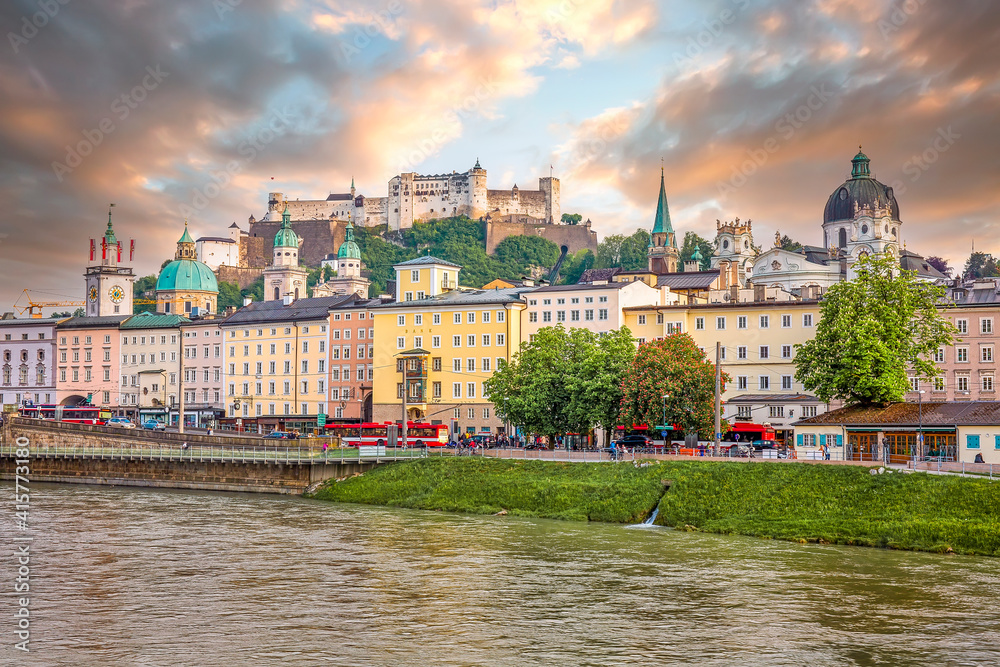 View to Hohensalzburg Fortress and Staatsbruecke bridge across Salzach river on a spring evening with many people walking