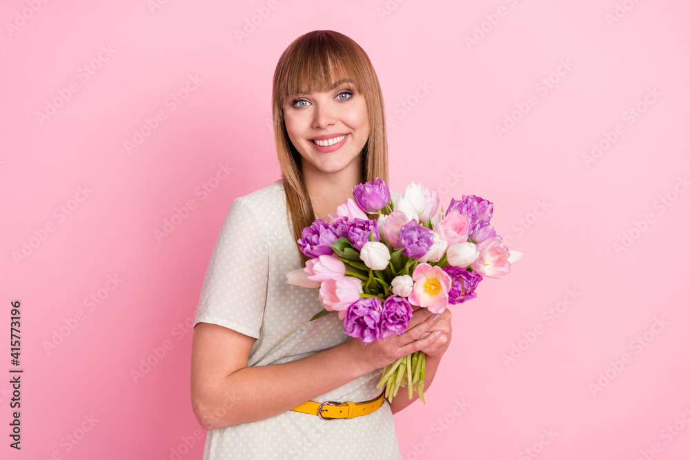 Portrait of attractive cheerful girl holding in hands flowers congrats festal occasion isolated over pink pastel color background