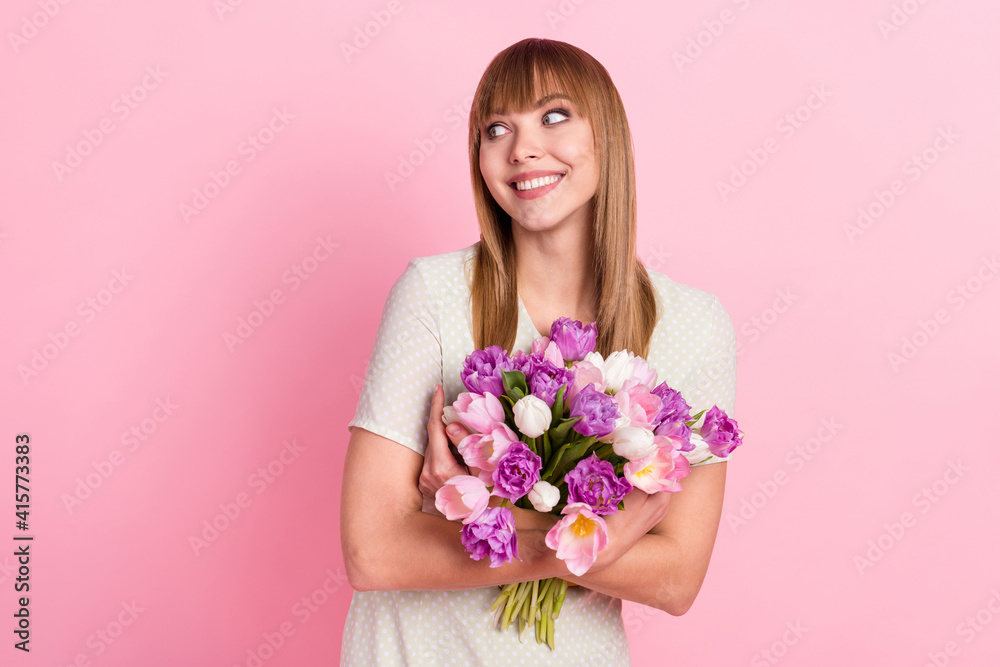 Portrait of pretty cheerful dreamy girl holding in hands hugging flowers congrats looking aside copy space isolated over pink pastel color background