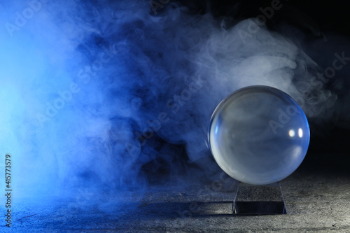 Magic crystal ball  on grey table and smoke against dark background, space for text. Making predictions photo